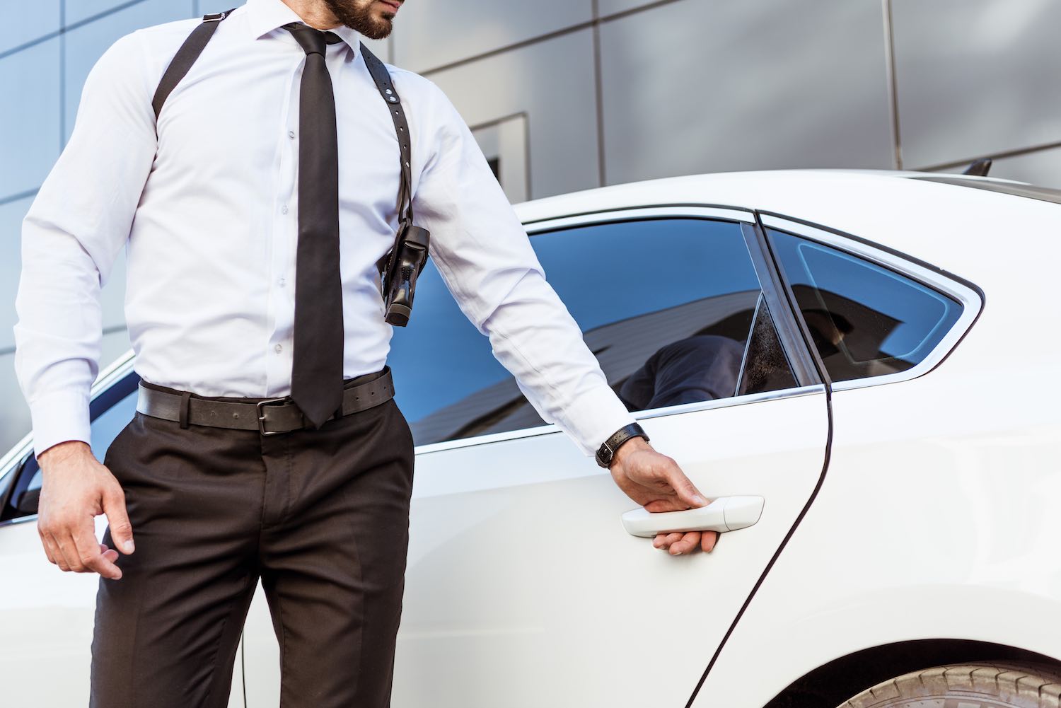 cropped image of security guard with gun opening car door